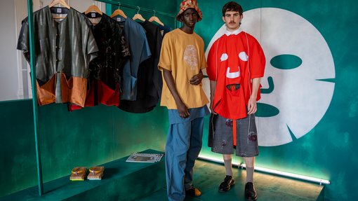 male model wearing a design next to a clothing rack