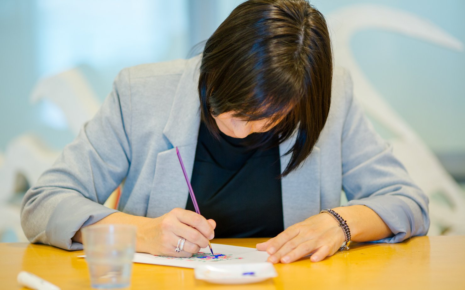 A photograph of a lady with her head down working on a painting