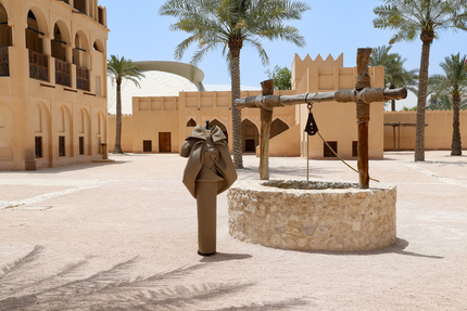 زي نحتي معروض بجانب بئر تقليدية في ساحة التراث بمتحف قطر الوطني.