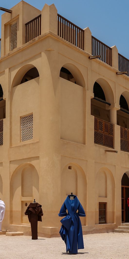 A traditional beige two-story building with four mannequins in colorful dresses displayed in the front, against a clear blue sky.