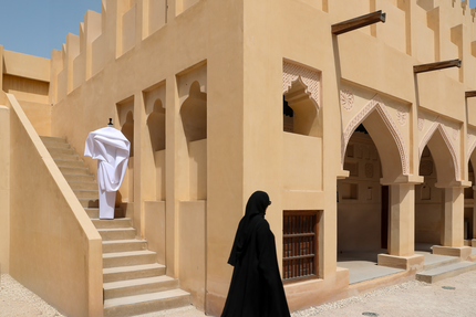 زي نحتي أبيض على درج في ساحة تراثية، بينما تمر امرأة ترتدي عباءة سوداء.