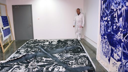 Visiting Artist Nedim Kufi in the corner of his studio at the Fire Station, looking at his painting laid on the floor of his studio.