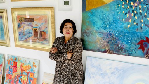 Ruwad Artist Wafika Sultan Al-Essa standing next to her paintings in her studio at the Fire Station.