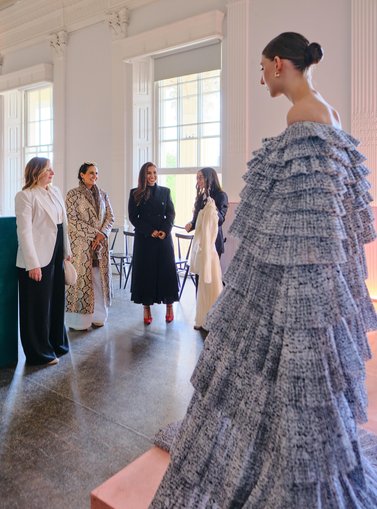 group of women talking and discussing a gown a model is wearing in front of them