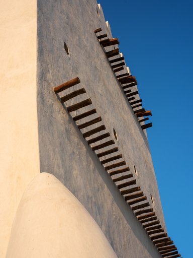 A close-up view of Barzan tower showing its white walls and protruding wooden shafts
