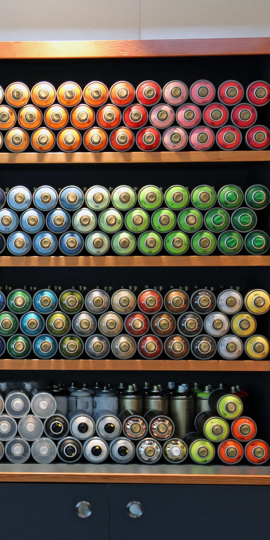 Interior of an artist supply shop with shelving, graphic signage and a rear wall displaying multiple rows of acrylic tubes of paint
