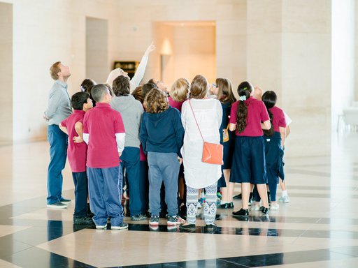 A photograph of a group of children standing in the lobby of MIA looking skywards