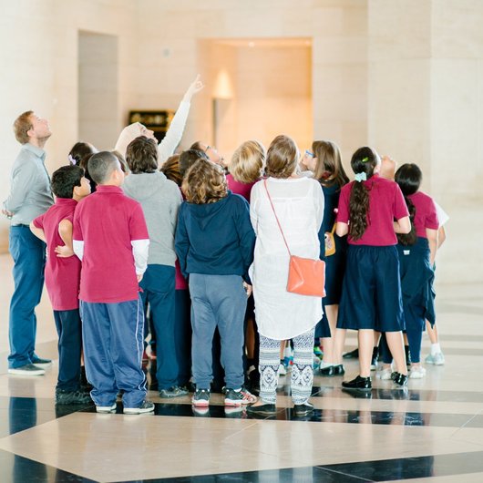 A photograph of a group of children standing in the lobby of MIA looking skywards