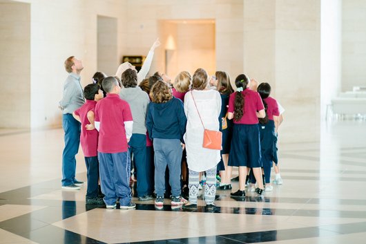 A photograph of a group of children standing in the lobby of MIA looking skywards