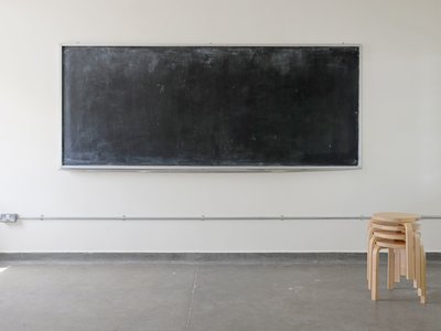 An empty white room with a blackboard on the wall and a pile of wooden stools.