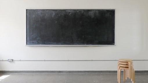 An empty white room with a blackboard on the wall and a pile of wooden stools.