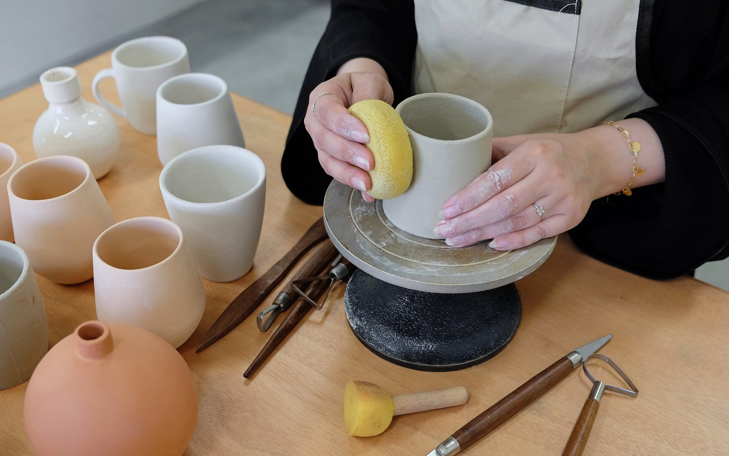 Close view of a woman making a pot in clay on a pottery wheel.