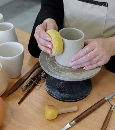 Close view of a woman making a pot in clay on a pottery wheel.