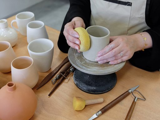 Close view of a woman making a pot in clay on a pottery wheel.