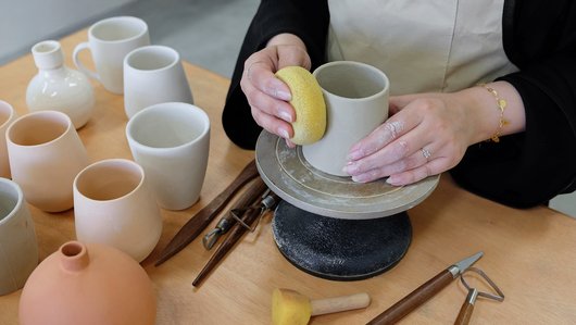 Close view of a woman making a pot in clay on a pottery wheel.