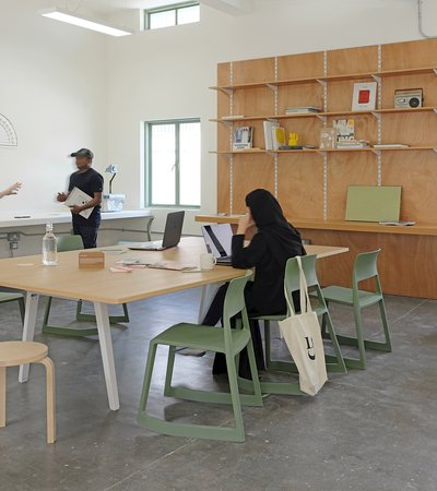 A modern interior space with large table and designer furniture with people sitting and standing.