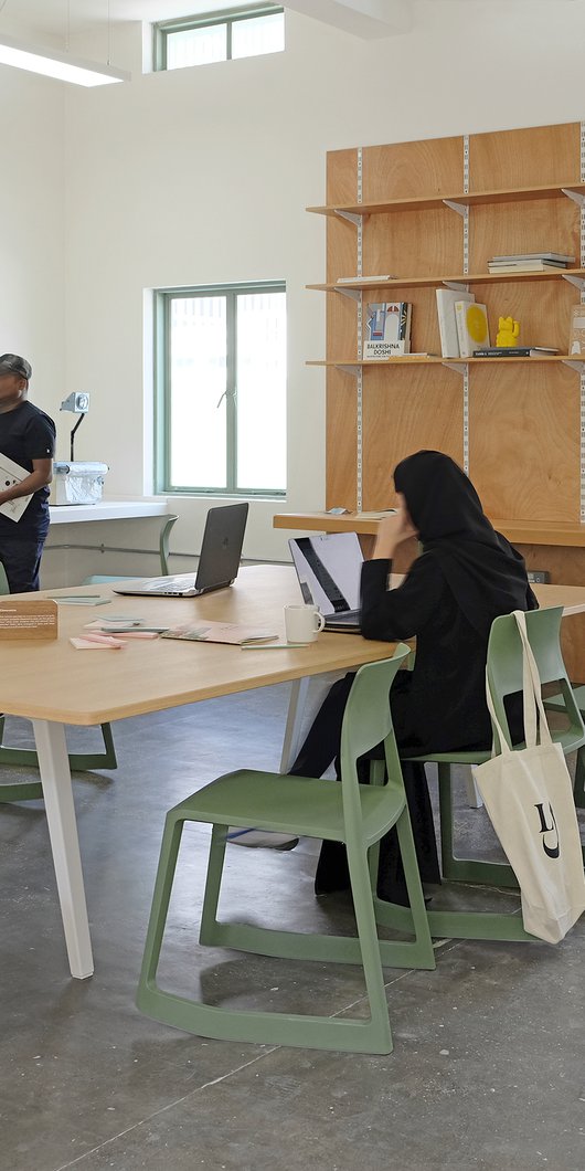 A modern interior space with large table and designer furniture with people sitting and standing.