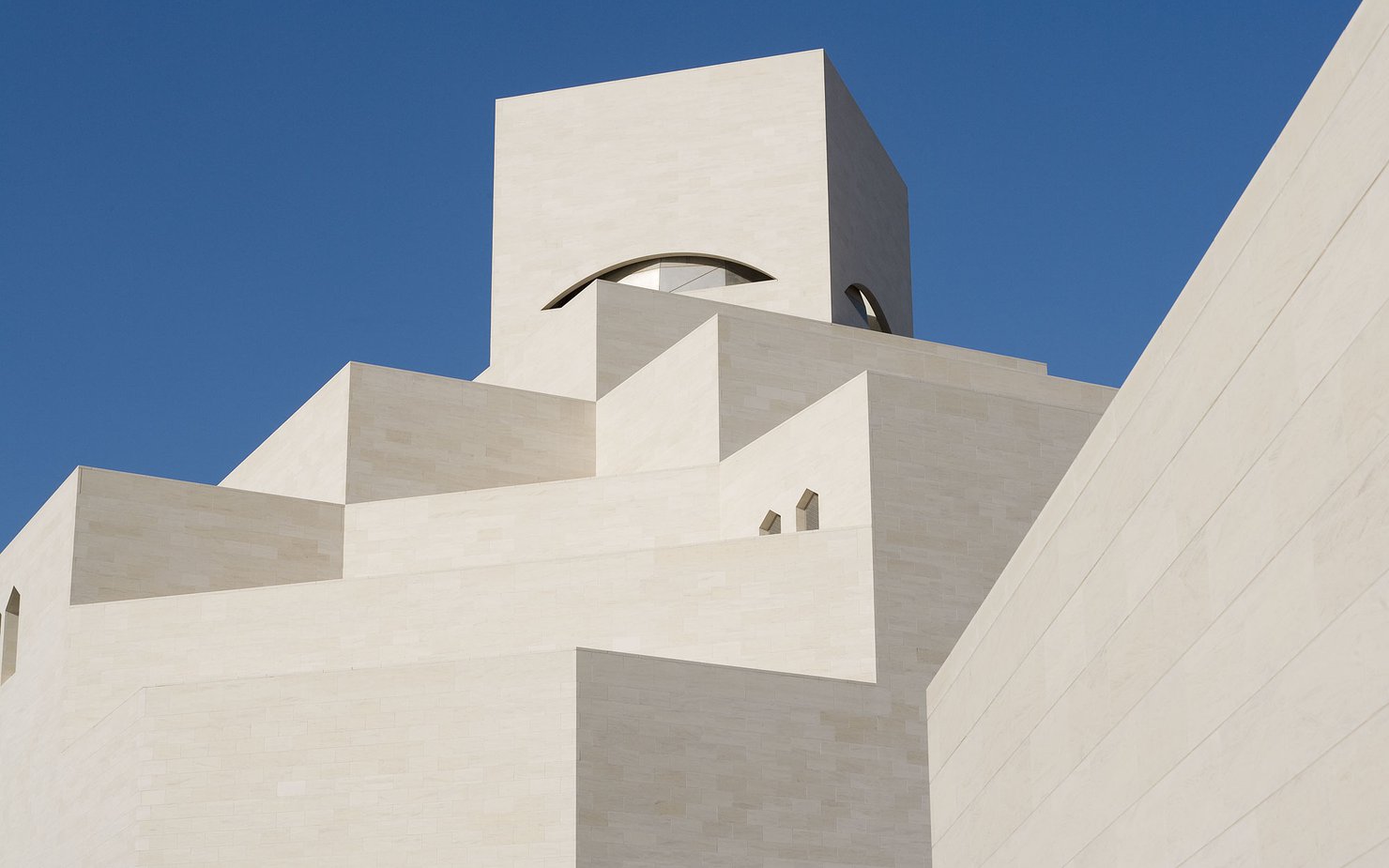 Detail of the white angular exterior of the Museum of Islamic Art with a blue cloudless sky in background