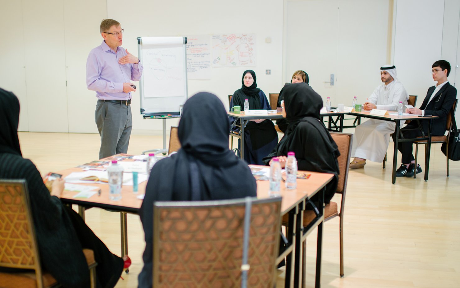 A teacher talks to adult students seated at desks