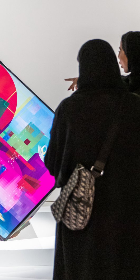 Two ladies in abaya viewing and pointing towards a digital artwork at the fire station gallery