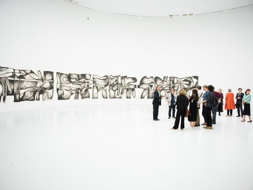 A group of visitors at the Al Riwaq's gallery space with works from Dia Al Azzawi's exhibition in the background