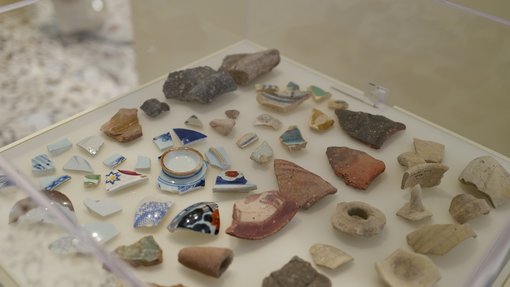 خزانة عرض تحتوي على قطع فخارية وسيراميك متنوعة بأشكال وألوان مختلفة مرتبة على سطح أبيض.