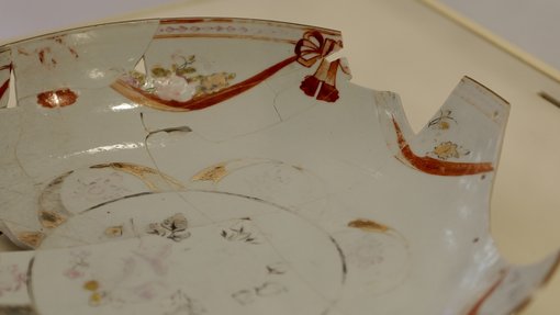 طبق خزفي مكسور مزين بنقوش زهرية ولمسات حمراء معروض على سطح بيج.