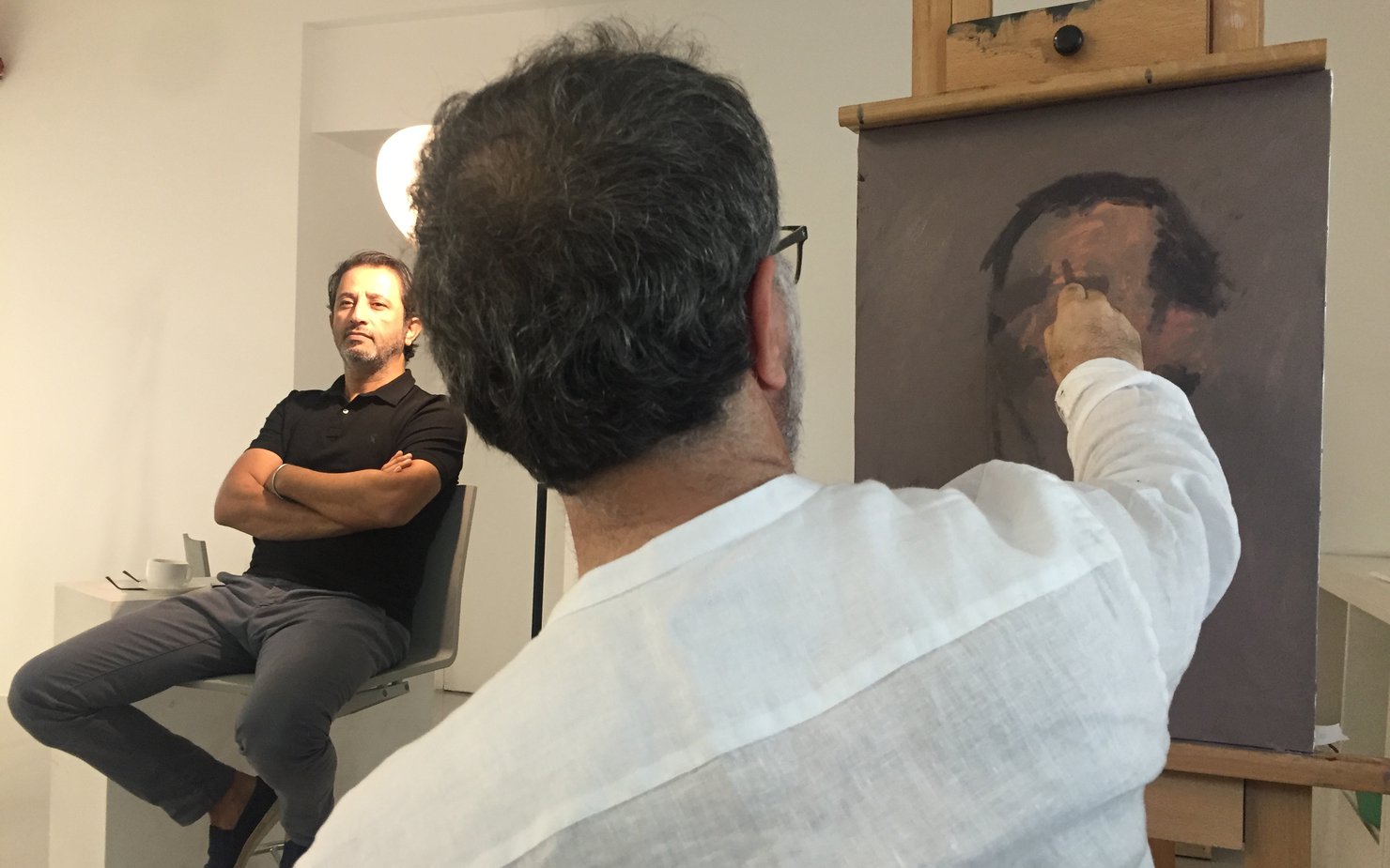 Ismail Azzam drafting a sketch of a man in the background posing under a lit lamp