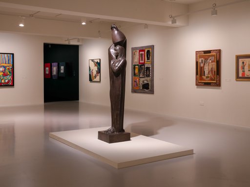 Photo of a gallery space with a sculpture of a peasant women with a jug on her head in the middle.