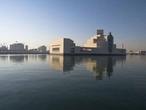An exterior view of the Museum of Islamic Art during the day, showing the building's reflection in the water