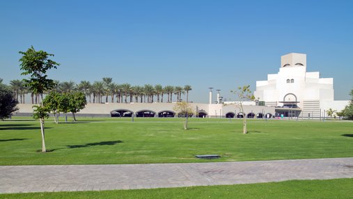 An open parkland space with green grass and native trees and the Museum of Islamic Art in the background