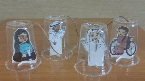 Drawing cutouts representing four characters in traditional Qatari costumes under plastic cups