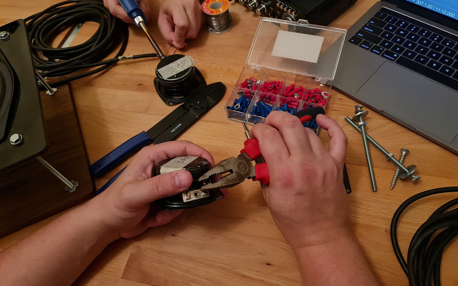 Two people working with pliers and cables alongside other tools and a laptop