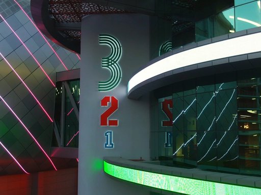 An image of neon lights highlighting the QOSM 3-2-1 signage