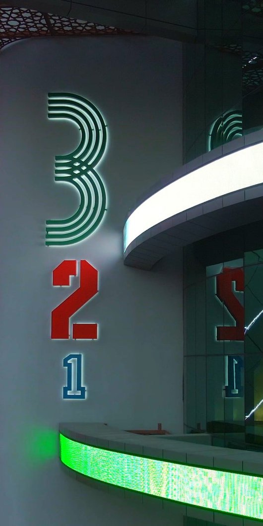 An image of neon lights highlighting the QOSM 3-2-1 signage