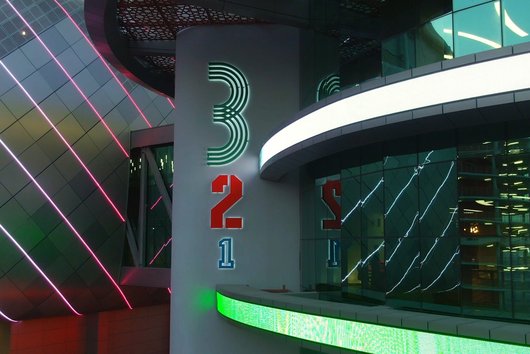 An image of neon lights highlighting the QOSM 3-2-1 signage