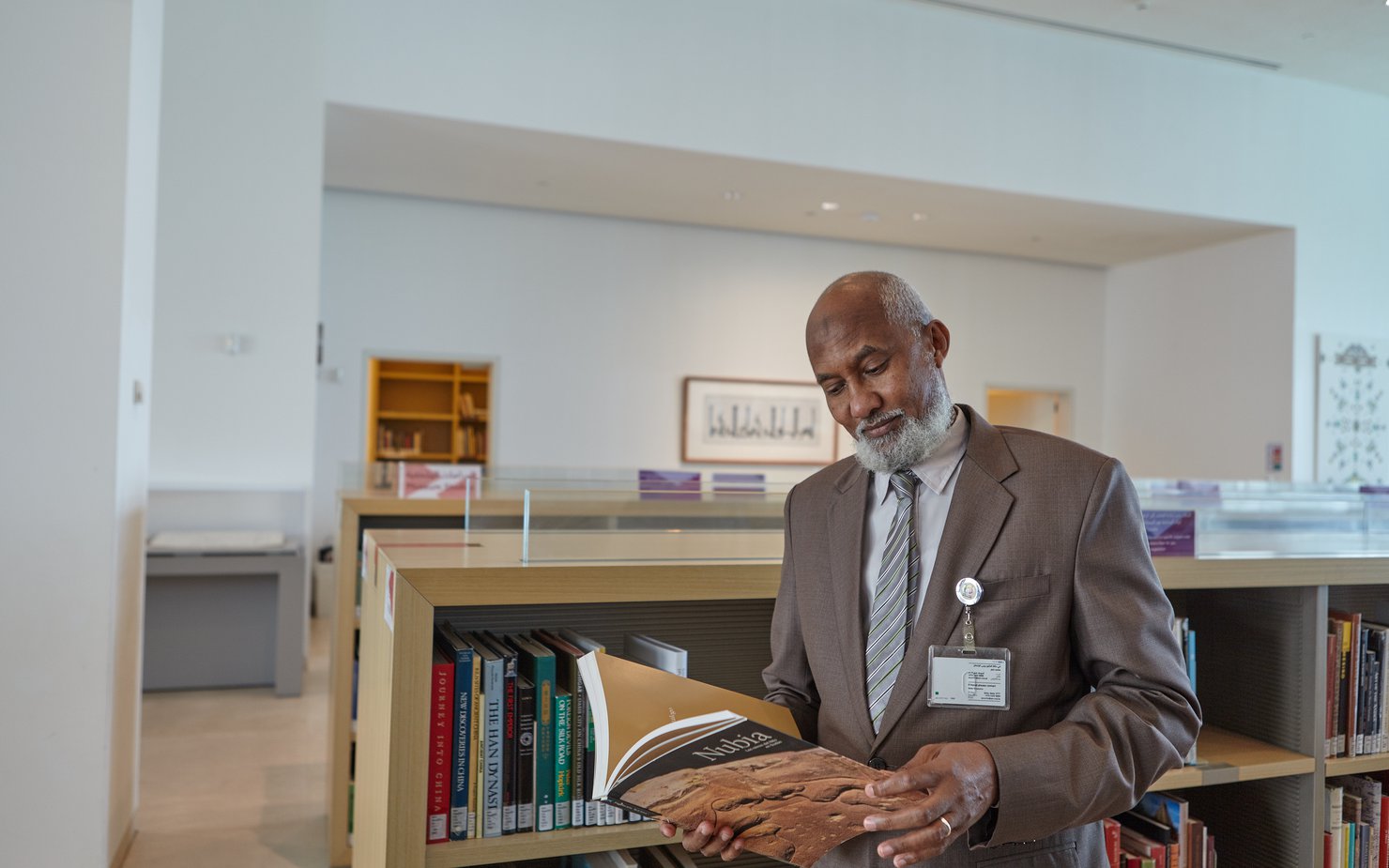 A man in a suit stands next to a bookshelf with a book in his hands