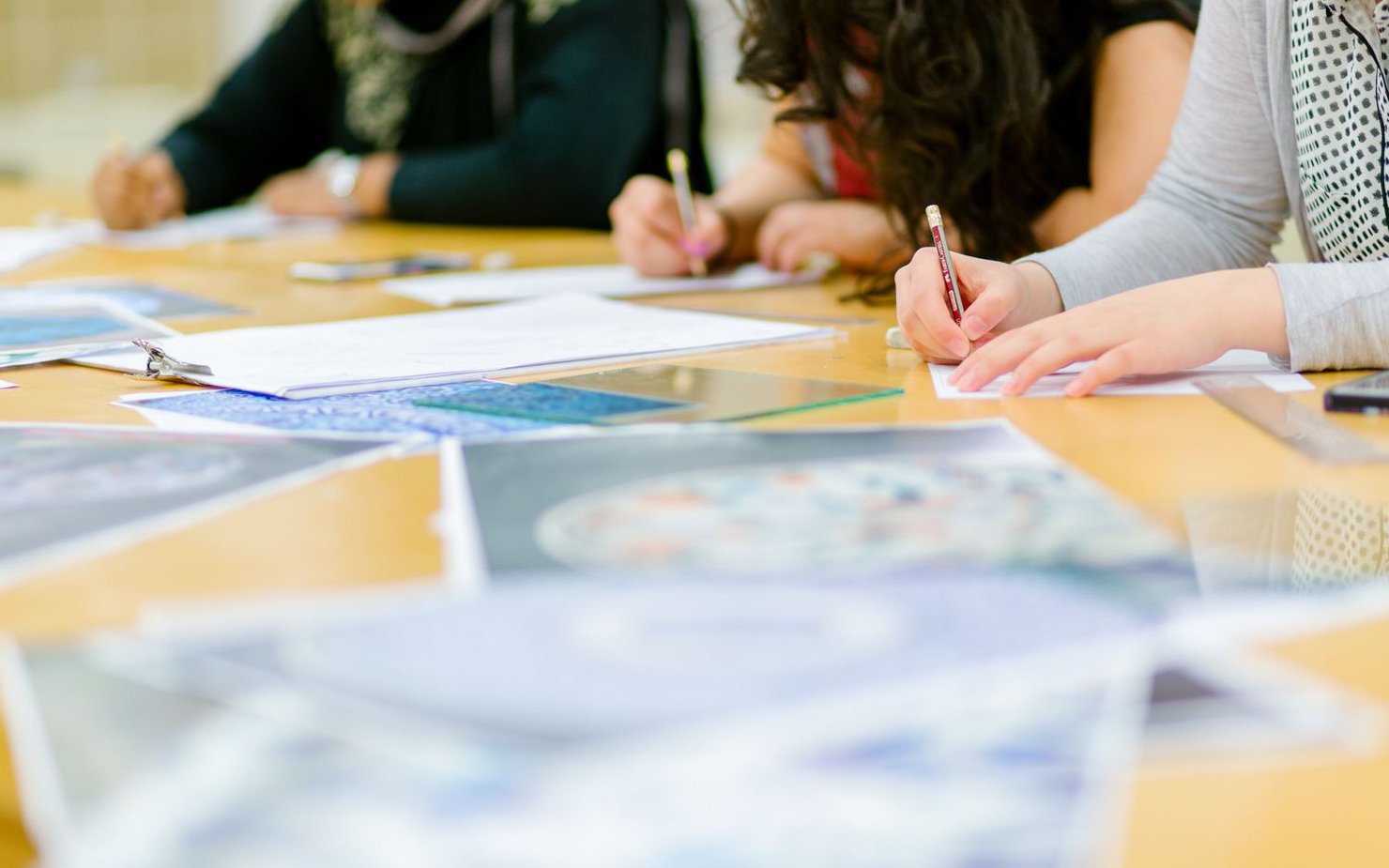 A shot of workshop participants sketching with pencils with scattered paper on the table.