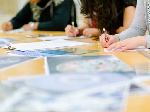 A shot of workshop participants sketching with pencils with scattered paper on the table.