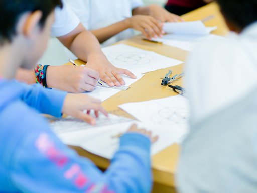 A group of children circled around a table, sketching out geometric shapes