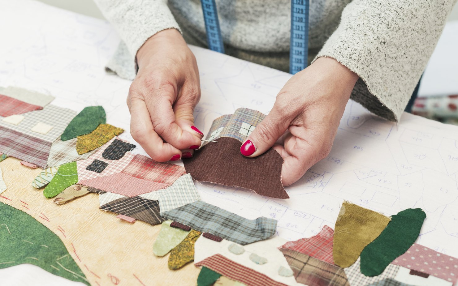 woman-s-hand-stitching-fabric-patch-house-with-needle-workplace
