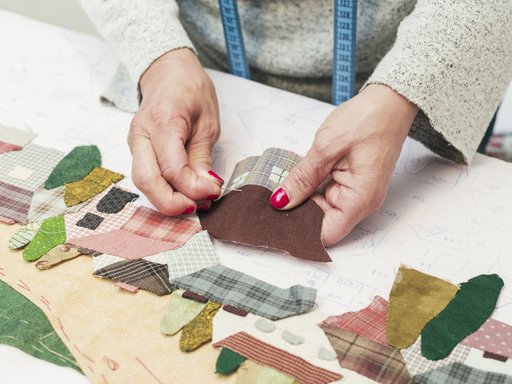 woman-s-hand-stitching-fabric-patch-house-with-needle-workplace